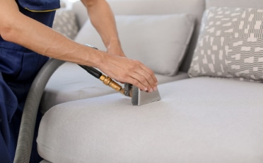 Man Using a Vacuum Cleaner to Clean a Grey Sofa — Upholstery & Carpet Cleaning on the Sunshine Coast, QLD