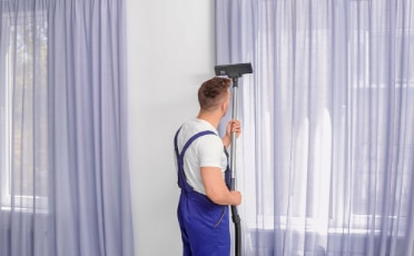 Man Using a Vacuum Cleaner to Clean a Purple Curtain — Upholstery & Carpet Cleaning on the Sunshine Coast, QLD