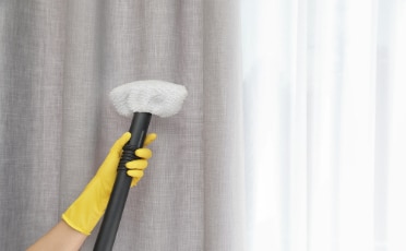 A Person Wearing Yellow Gloves Holding a Curtain Cleaning Tool — Upholstery & Carpet Cleaning on the Sunshine Coast, QLD