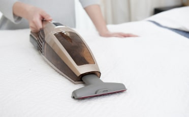 A Woman Using a Vacuum Cleaner on A Mattress — Upholstery & Carpet Cleaning on the Sunshine Coast, QLD